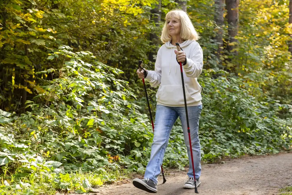 Una signora cammina con i bastoncini lungo un sentiero nel bosco
